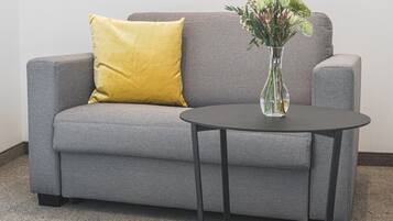 A grey sofa with a yellow pillow and a clear vase with flowers on a small round table.
