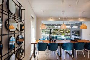 A modern dining area with a wooden table, blue chairs, and pendant lights. - Sauna, heated pool, kids pool, close to the beach & shops! (Rethymno)