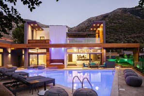 A modern two-story house with a swimming pool, outdoor seating, and a mountain backdrop. - Sauna, heated pool, kids pool, close to the beach & shops! (Rethymno)