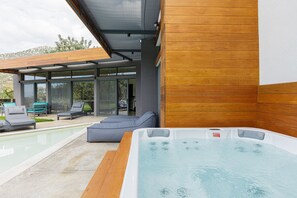 A modern outdoor pool area with a hot tub, lounge chairs, and a covered seating area.