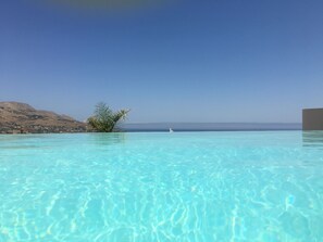 Une piscine d’un bleu éclatant, avec vue sur une côte lointaine et une petite île parsemée de palmiers.