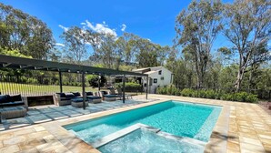 A rectangular swimming pool with a pergola and lounge area, surrounded by a stone deck and trees. - Marlu Station - Secluded family getaway in Broke (Broke)