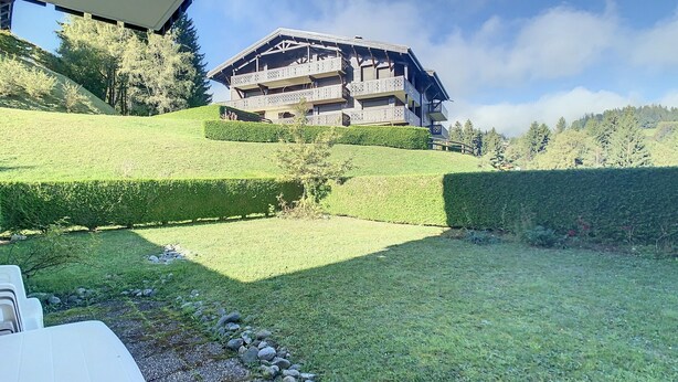 A multi-story building with balconies, surrounded by well-manicured lawns and hedges, set against a backdrop of trees and hills. - Cozy cabin studio near ski lift (Combloux)