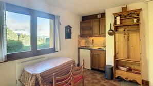 A compact kitchen with wooden cabinets, a built-in stove, and a window overlooking greenery. - Cozy cabin studio near ski lift (Combloux)