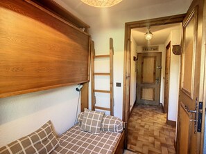 A narrow hallway with a wooden bench and a ladder, leading to a door.