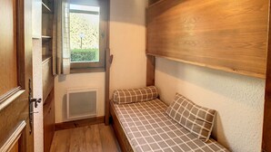 A small, cozy room with a bed, a window with curtains, a wooden headboard, and a ceiling light. - Cozy cabin studio near ski lift (Combloux)