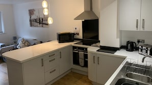 A modern kitchen with white cabinetry, a built-in oven, a microwave, and a sink with a dish rack. - Stylish and Immaculate 2-bed Apartment in Leigh (Leigh)