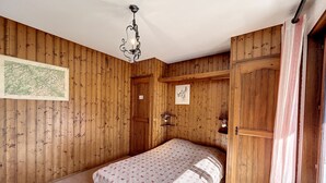 Ein Zimmer mit Holzwänden, einem Bett mit gemustertem Überwurf, einer Pendelleuchte und einer Tür mit Spiegel.