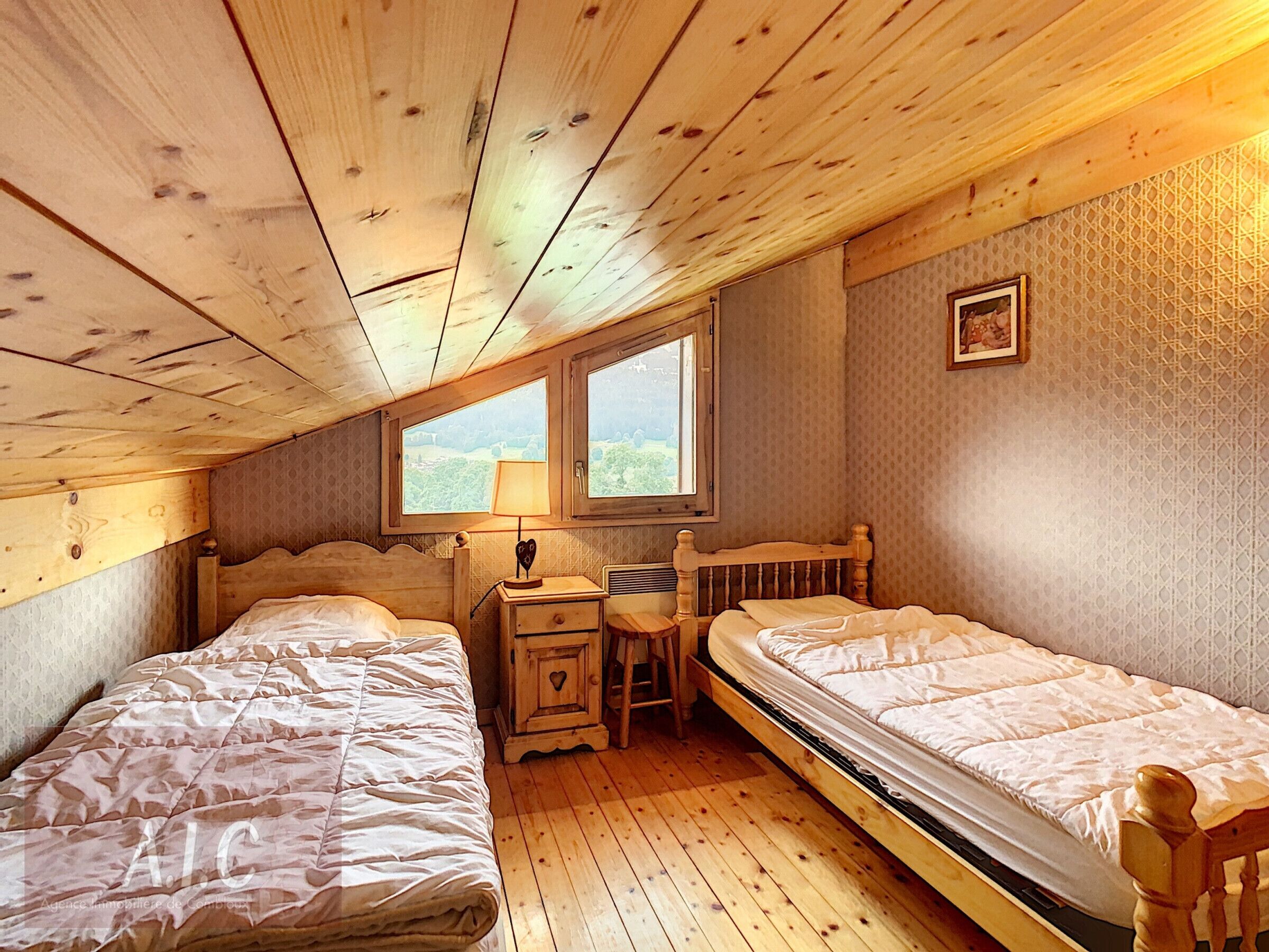A cozy room with two wooden beds, a small desk, and a window providing a view of greenery.