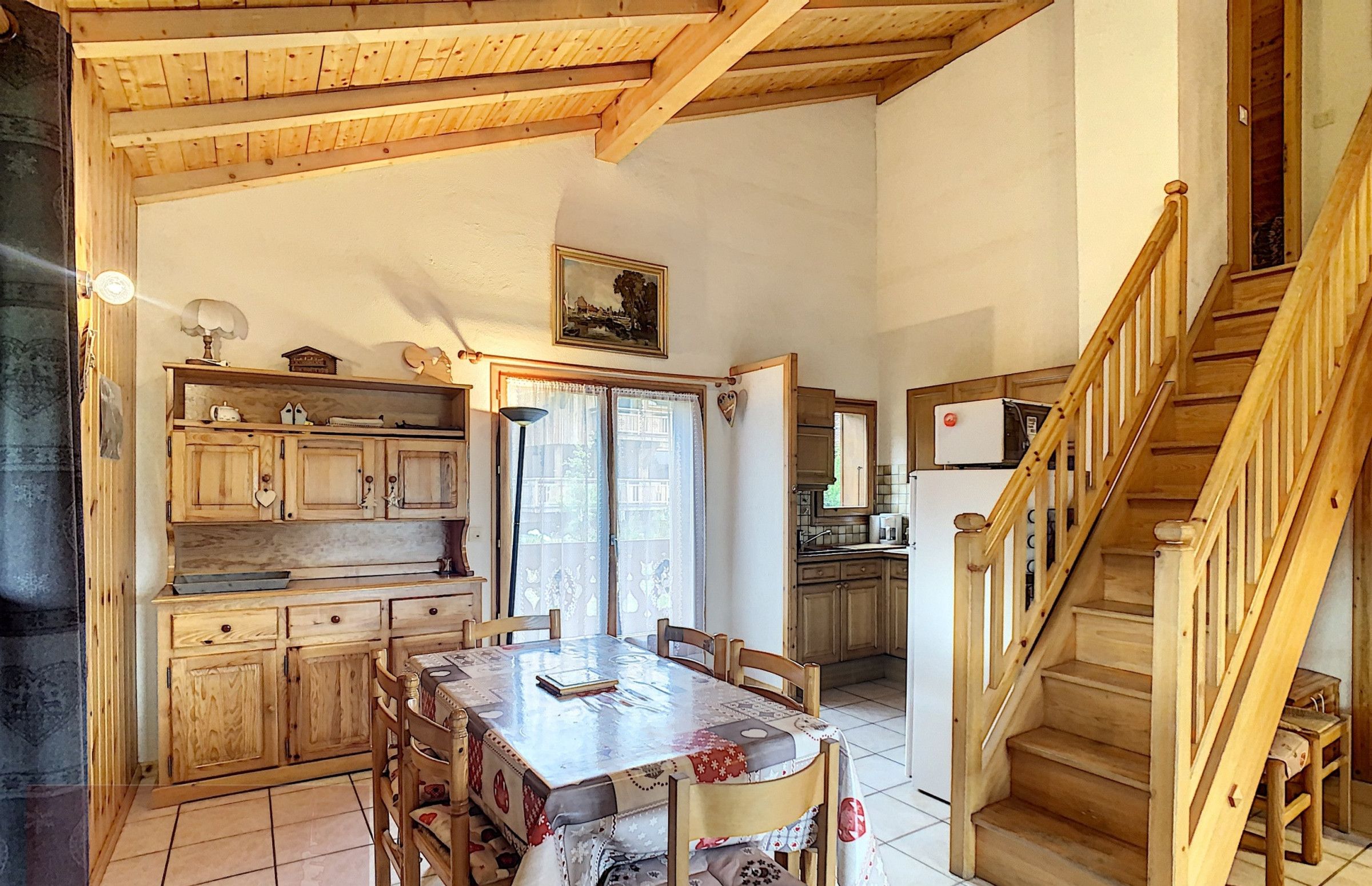 A rustic kitchen with wooden cabinets and a dining table set for four. A staircase leads to an upper level.