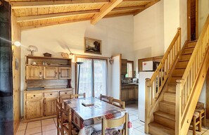 A rustic kitchen with wooden cabinets and a dining table set for four. A staircase leads to an upper level. - Spacious 110m² Duplex 3 Bedrooms with Balcony & Terrace (Combloux)