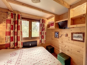 A cozy wooden cabin room with a bed, a TV, and two small stools. - Charming duplex near Bouchet ski lift, ideal for family (Combloux)