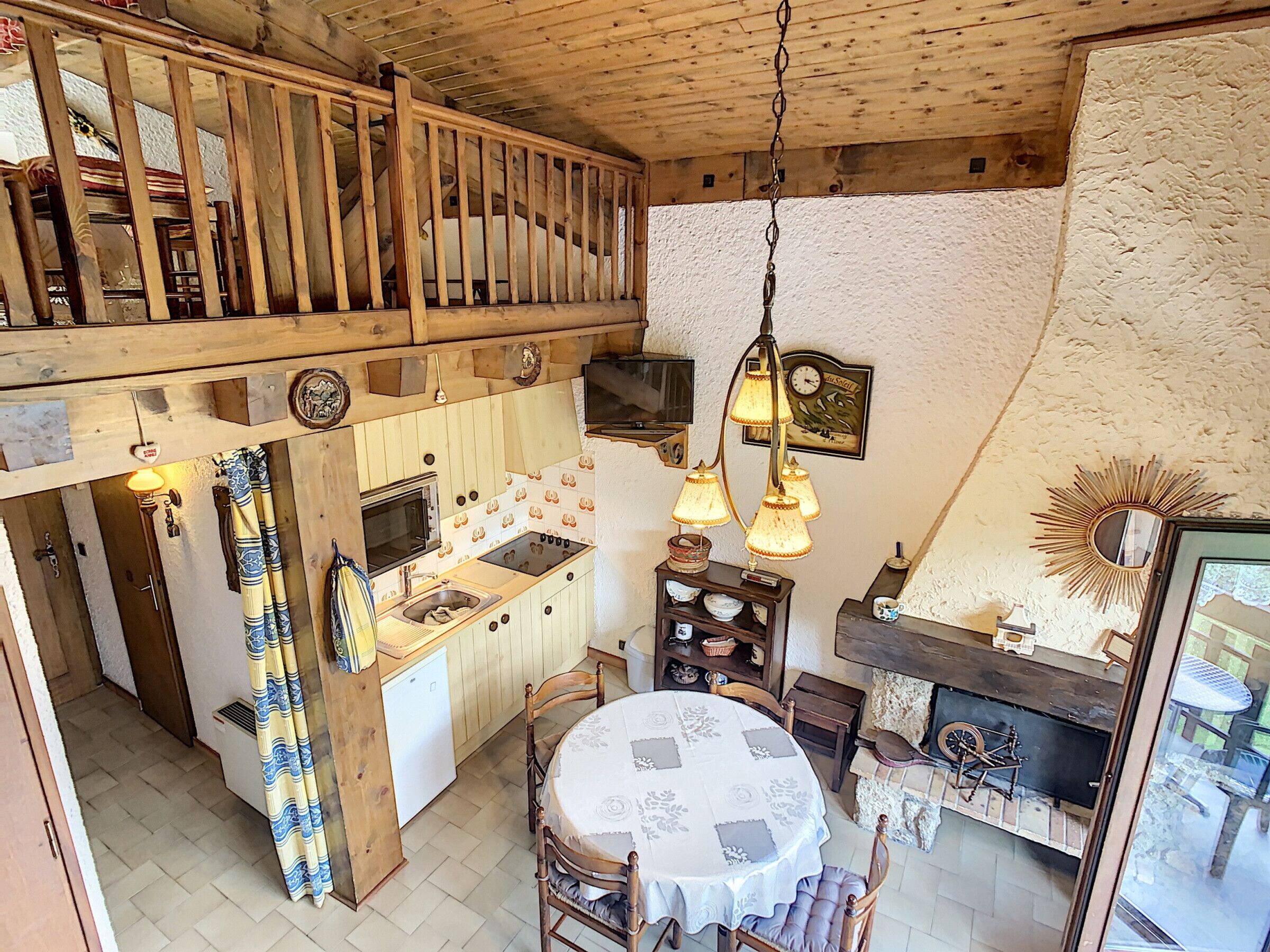 A rustic kitchen with wooden beams, a dining area with a round table, and a fireplace.