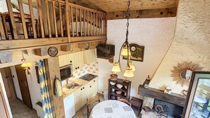 A rustic kitchen with wooden beams, a dining area with a round table, and a fireplace. - Cozy duplex 35m² near Combloux center, facing Mont Blanc (Combloux)
