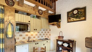 A compact kitchen with wooden cabinets, a microwave, a sink, and a dining area with a table and chairs. - Cozy duplex 35m² near Combloux center, facing Mont Blanc (Combloux)