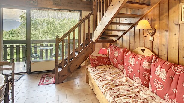 A cozy room with a wooden staircase, a sofa with heart patterns, and a view of greenery outside. - Cozy duplex 35m² near Combloux center, facing Mont Blanc (Combloux)