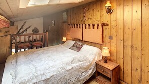 A cozy bedroom with a sloped ceiling, wooden walls, a bed with a white bedspread, two bedside lamps, and a wooden nightstand. - Cozy duplex 35m² near Combloux center, facing Mont Blanc (Combloux)