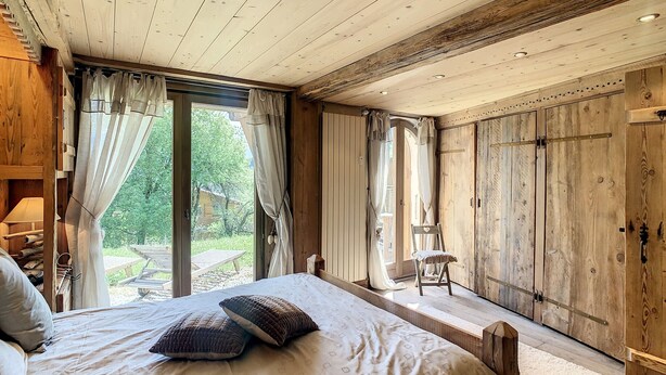 A bedroom with a large bed, wooden walls, and a sliding door to a balcony.