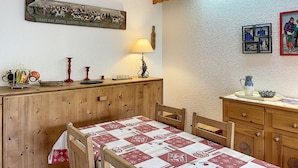 A dining area with a wooden table and chairs, a wall-mounted lamp, and a decorative plate with a pastoral scene. - Charming 2-room apartment in Combloux center with balcony (Combloux)