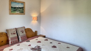 A bedroom with a bed, a nightstand, a wall-mounted lamp, and a framed picture. - Charming 2-room apartment in Combloux center with balcony (Combloux)