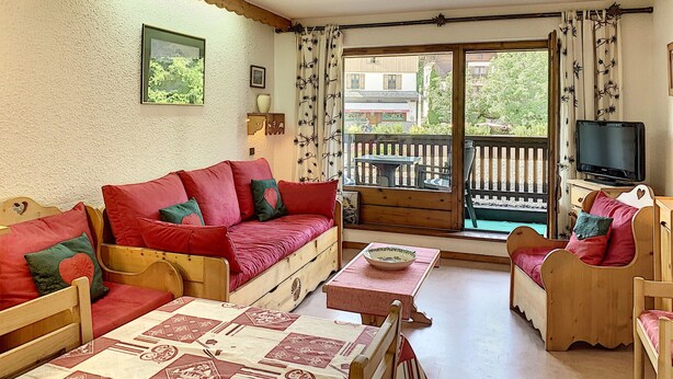 A cozy room with a wooden sofa, a small table, and a television. - Charming 2-room apartment in Combloux center with balcony (Combloux)