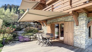 A wooden deck with a table and chairs, stone walls, and a wooden pergola.