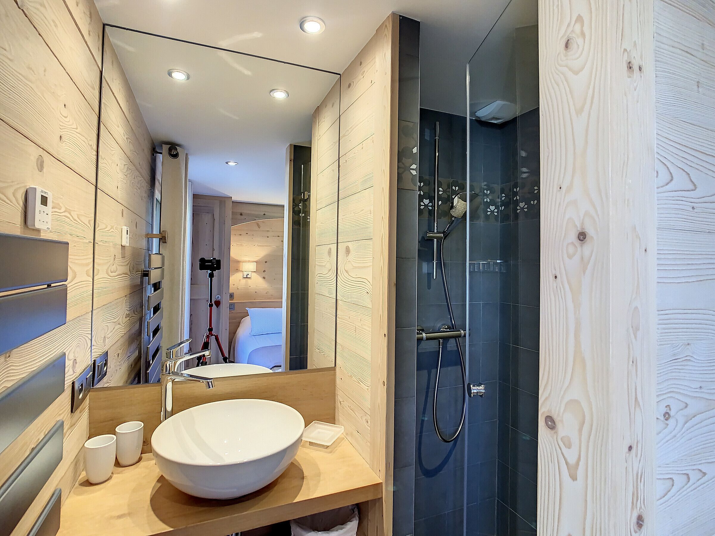 A modern bathroom with a large white sink, a glass-enclosed shower, and wooden paneling.