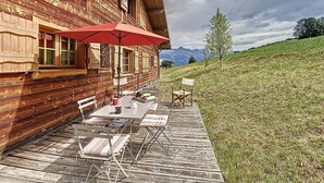 Una cabaña de madera con patio, mobiliario exterior y vistas a la montaña.