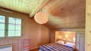 Un dormitorio de cabaña de madera con una cama, una lámpara colgante, una ventana y una puerta.