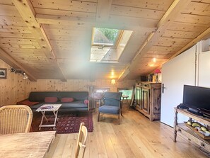 L’intérieur chaleureux d’un chalet avec un plafond en bois, un canapé, une table à manger, un téléviseur et un coin cuisine.