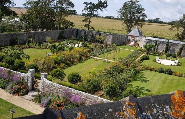 A well-maintained garden with a stone wall, a small building, and a field in the background.