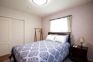 Un dormitorio con una cama, una mesita de noche con lámpara, un perchero y una ventana con cortinas.