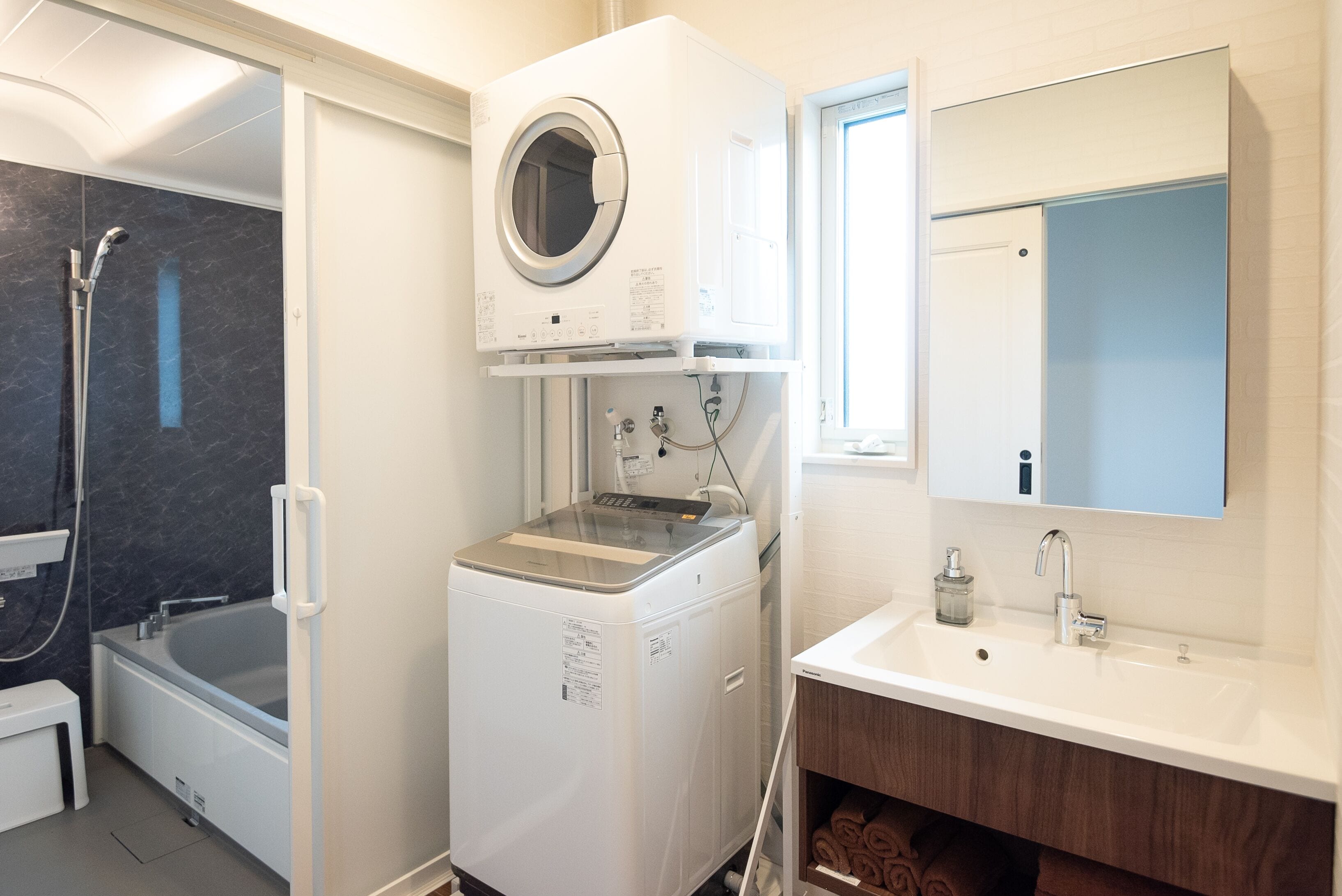 A compact bathroom with a built-in washer and dryer, a separate shower area, and a vanity with a mirror.