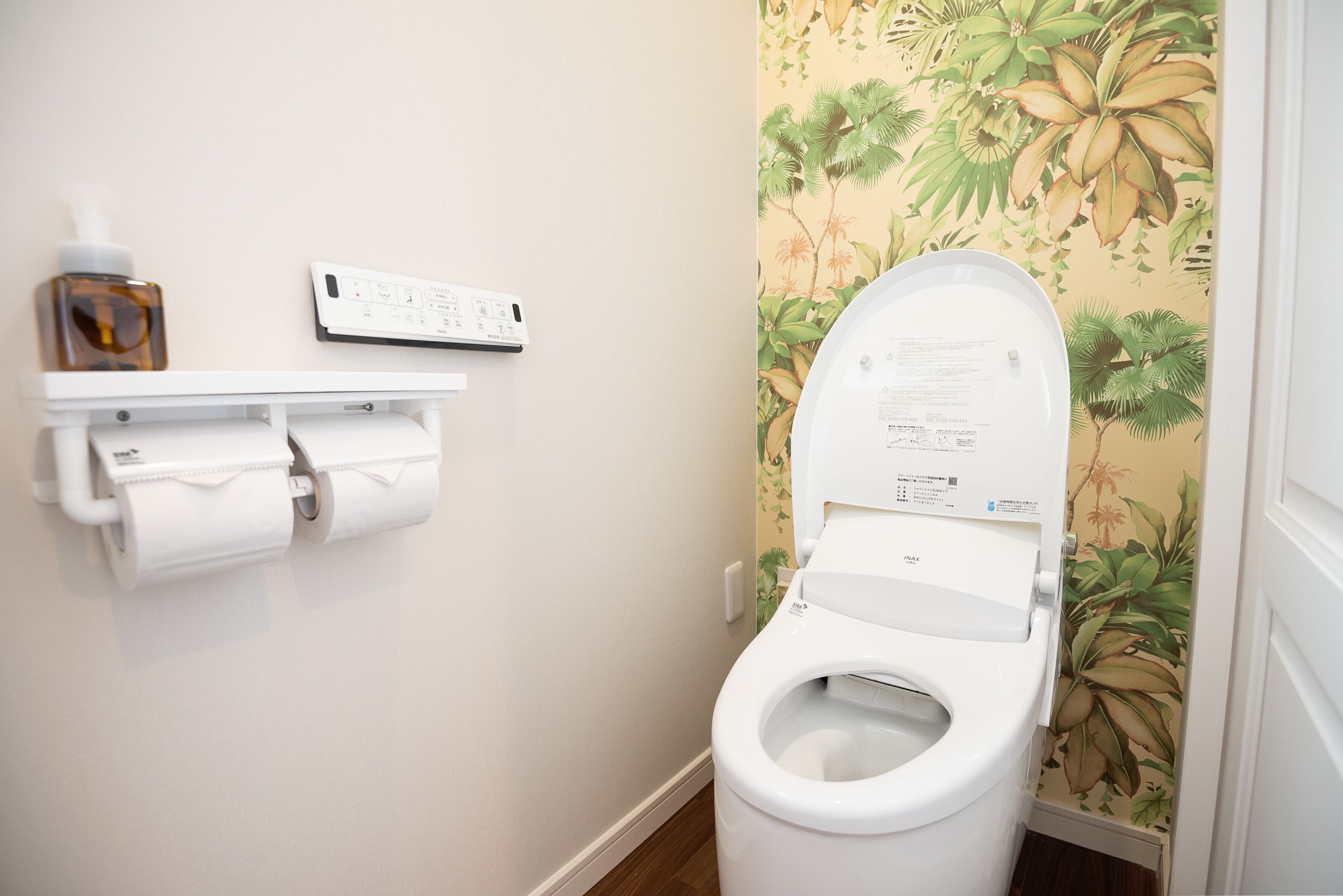 A toilet with a flush handle, a toilet paper holder, and a wall-mounted electrical outlet.