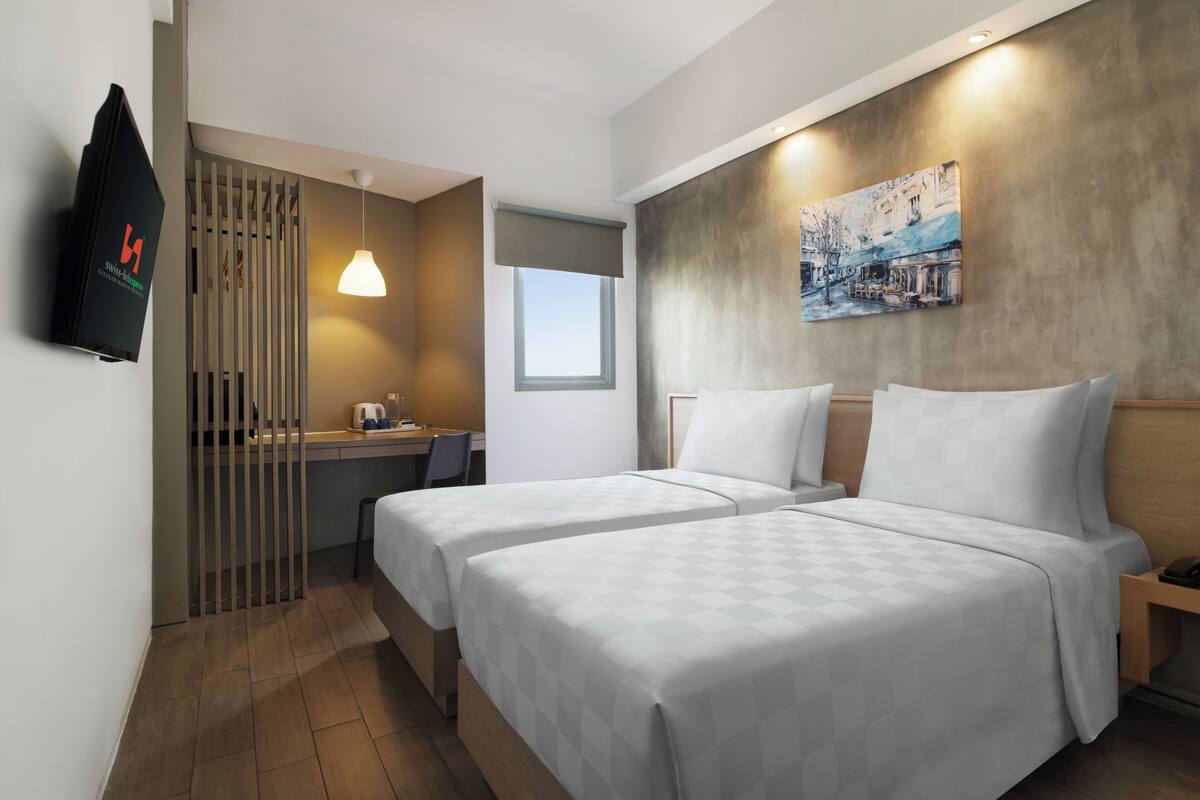 Ein Hotelzimmer mit zwei Betten, einem Schreibtisch, einem Sessel, einem Fernseher und einem Bild an der Wand.
