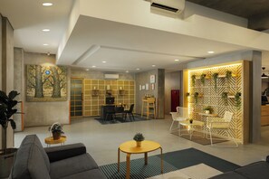 A modern hotel lobby with a seating area, a reception desk, and a wall with a geometric pattern and greenery.