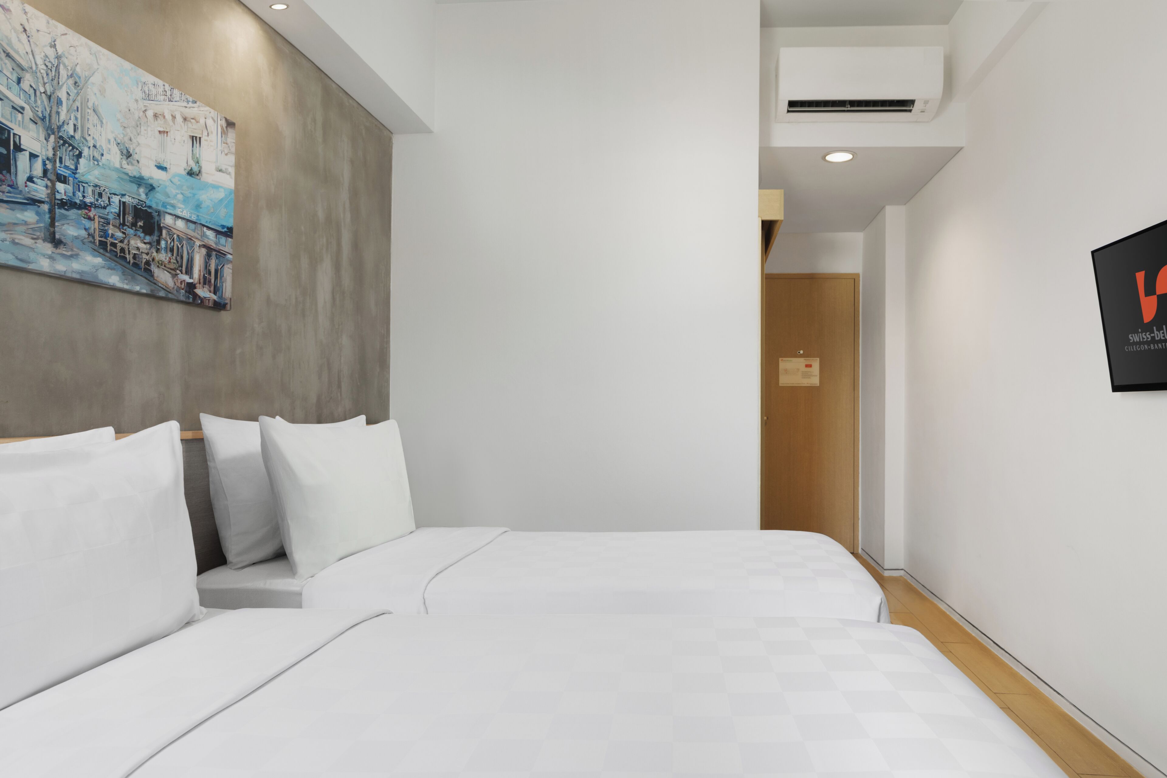 A modern hotel room with a large bed, a painting on the wall, and a logo on the wall.