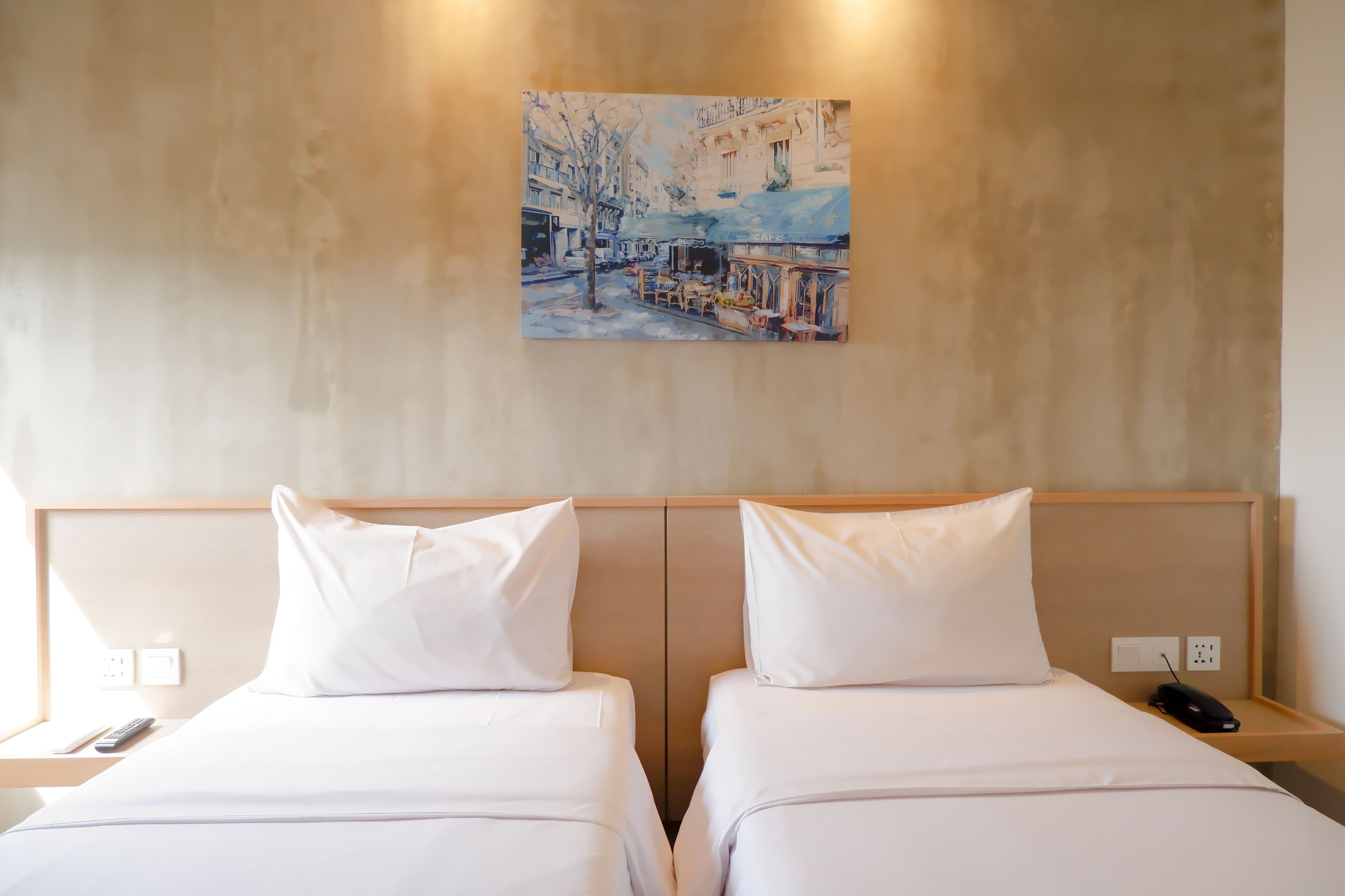 A hotel room with two beds, a painting on the wall, and a bedside table with a remote control.