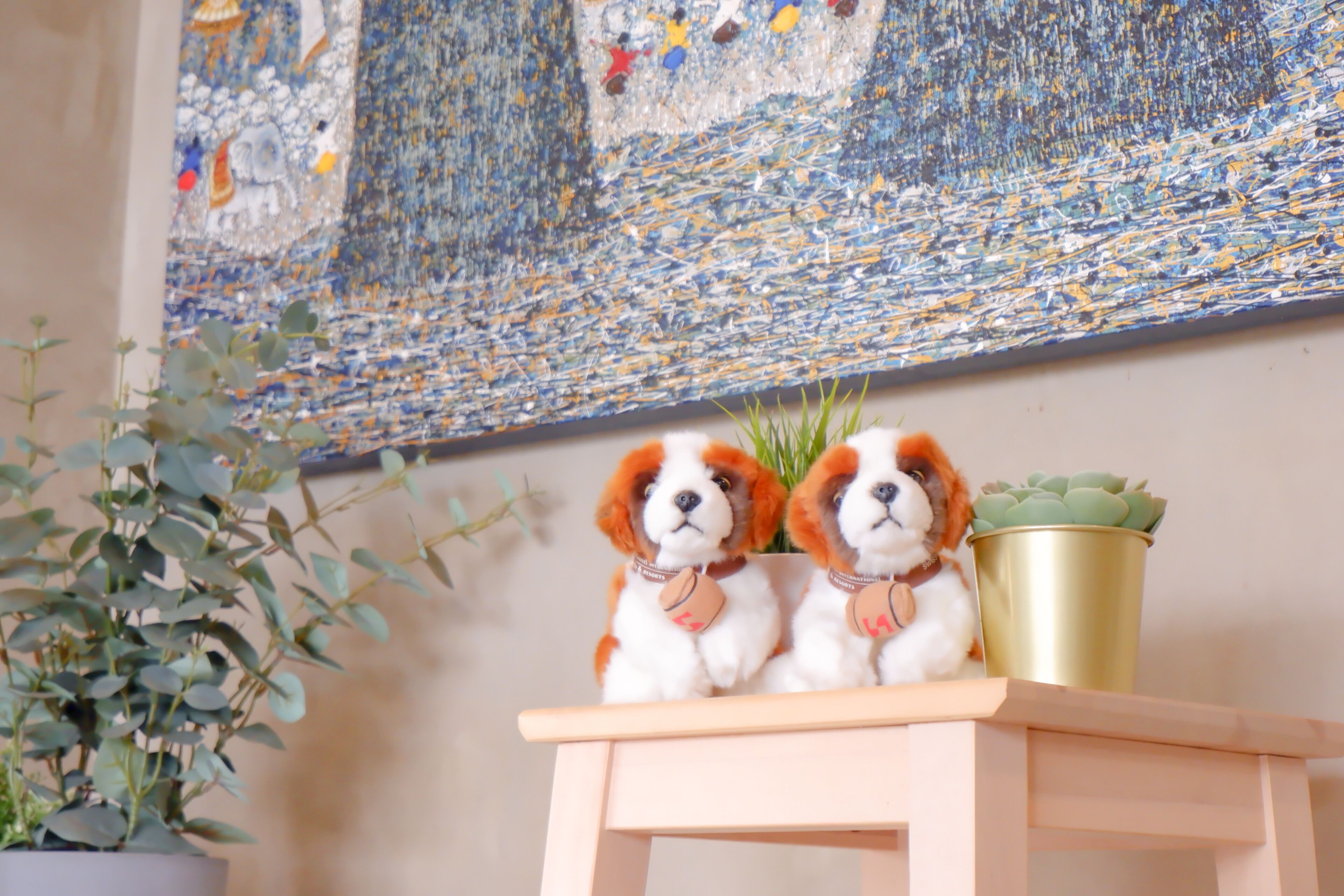 Two dogs sitting on a small wooden table with a potted plant beside them.