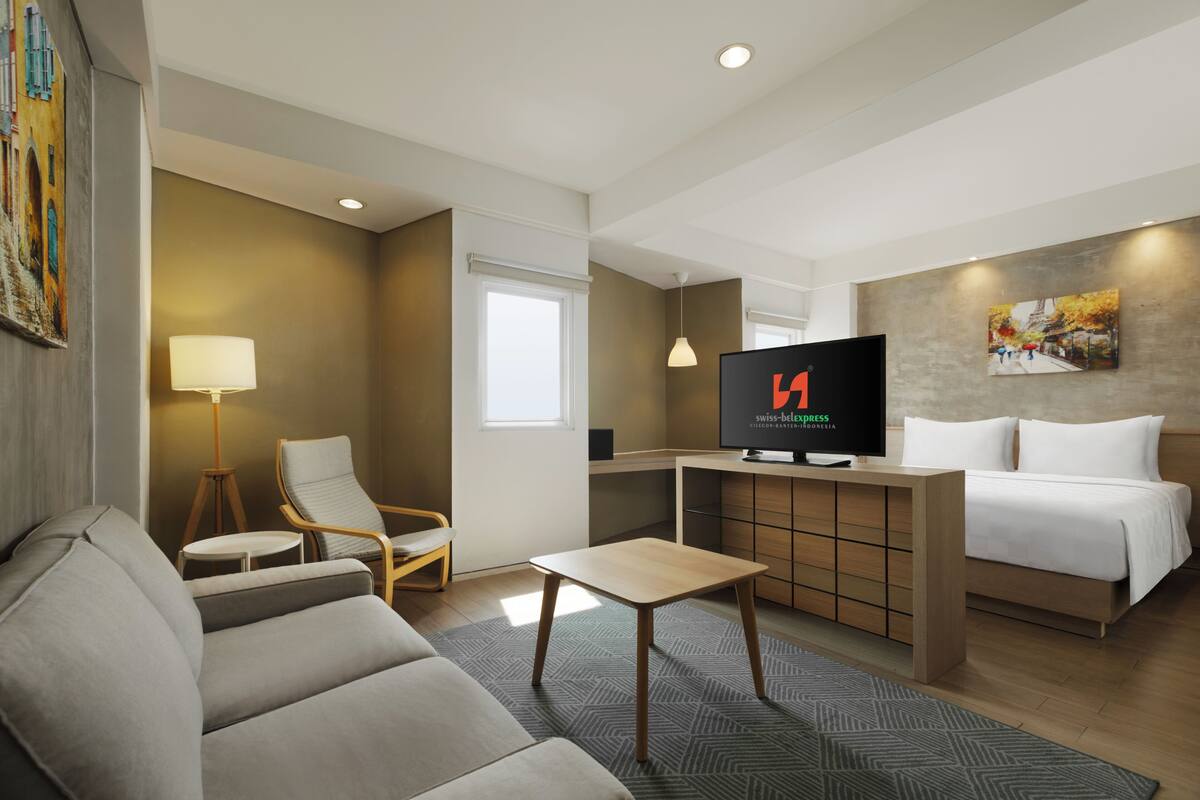 Ein Hotelzimmer mit Sofa, kleinem Tisch, Fernseher, Bett und Schreibtisch.