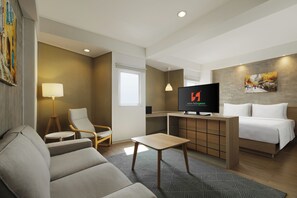 A hotel room with a sofa, a small table, a TV, a bed, and a desk.