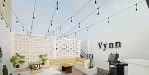 A modern outdoor seating area with a white wall, a sofa, a table, and string lights.