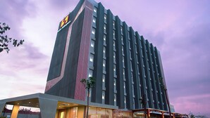 Un hotel moderno con una fachada geométrica llamativa, varios pisos y un área exterior bien cuidada con plantas y un sendero.