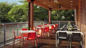 Un área de comedor al aire libre con mesas y sillas, techo de madera y vistas a árboles.