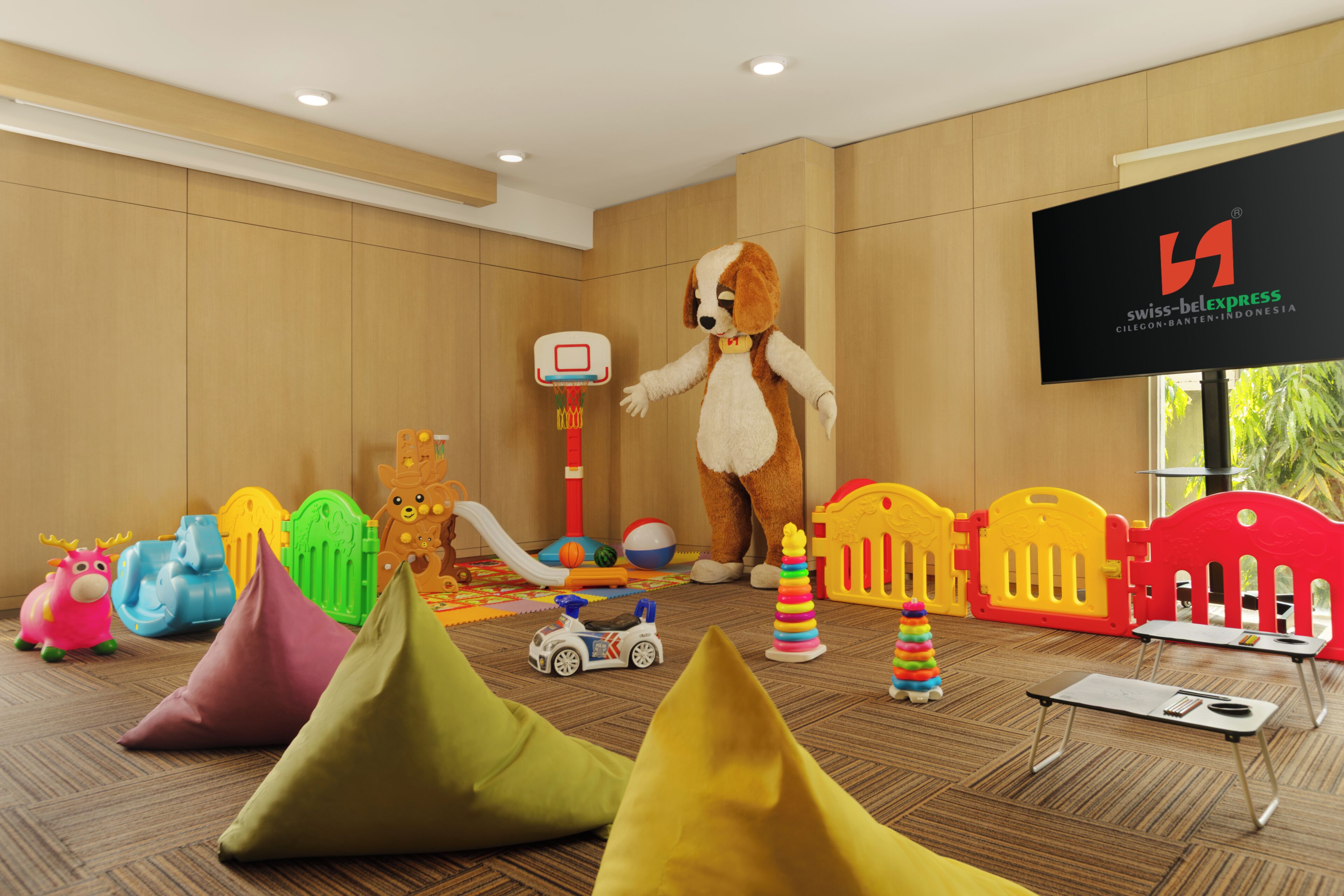 A room with a mascot, a basketball hoop, colorful play structures, and a Swiss-Belexpress sign.