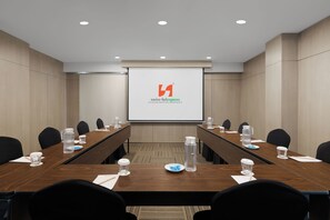 A conference room with a long table, chairs, a projector screen, and a logo. - Swiss-Belexpress Cilegon (Cilegon)
