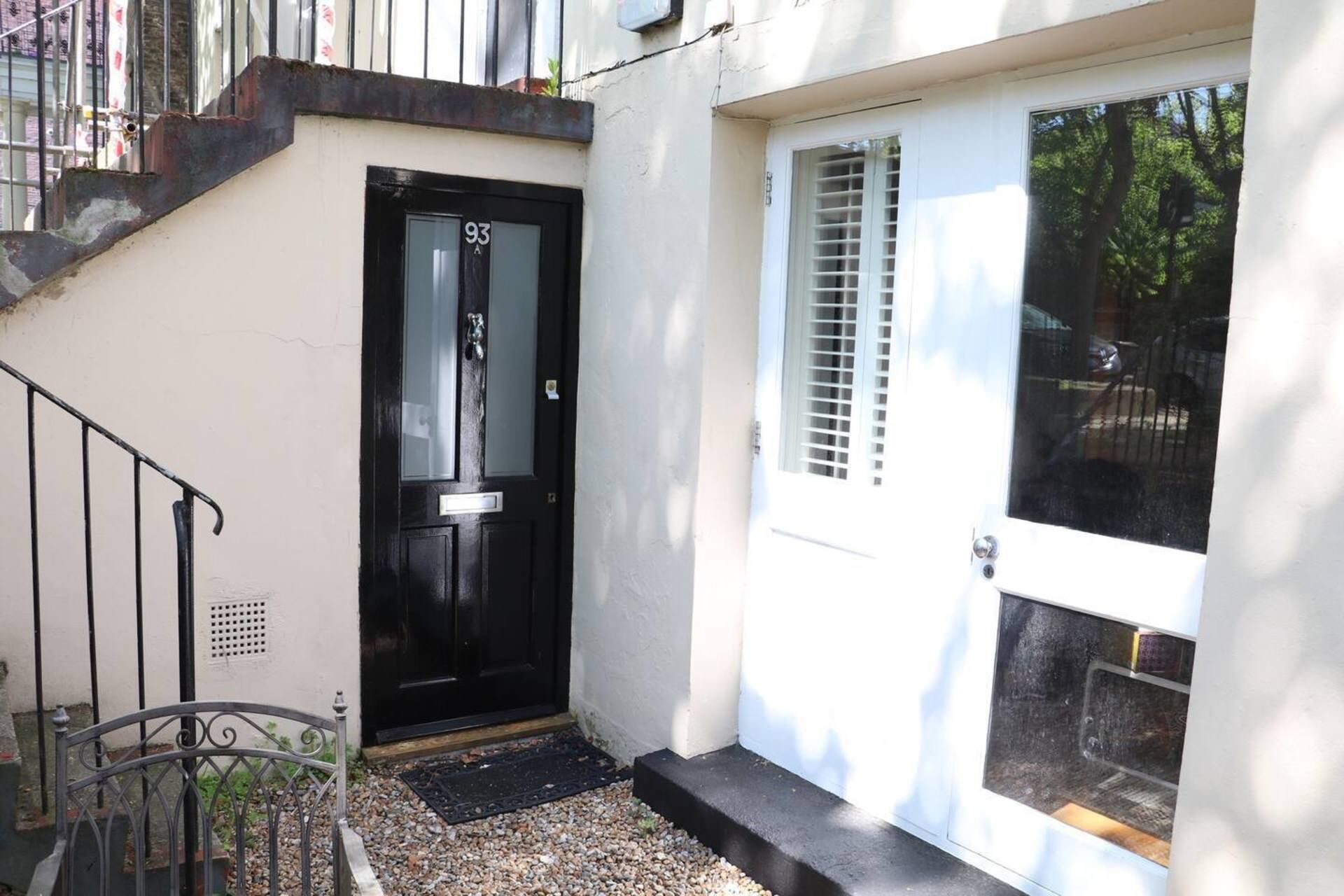 A black door with a small step leading to a white door with a window.