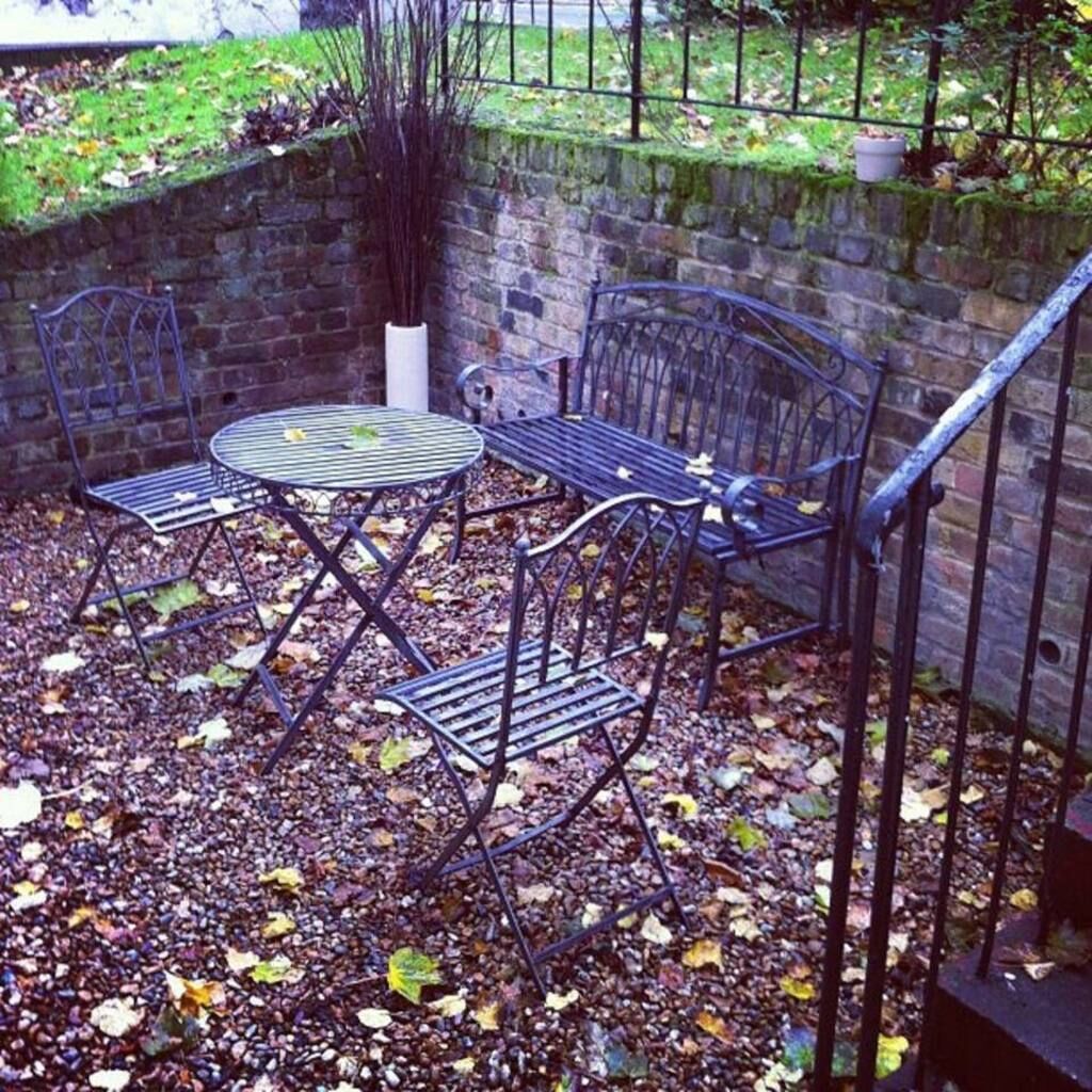 Ein Patio mit einem runden Metalltisch und vier Stühlen, umgeben von einer Steinmauer und einem Metallzaun.