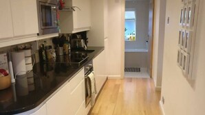 A modern kitchen with white cabinets, a black countertop, and a microwave. - 2-bed, Sleeps 4, Garden (London)