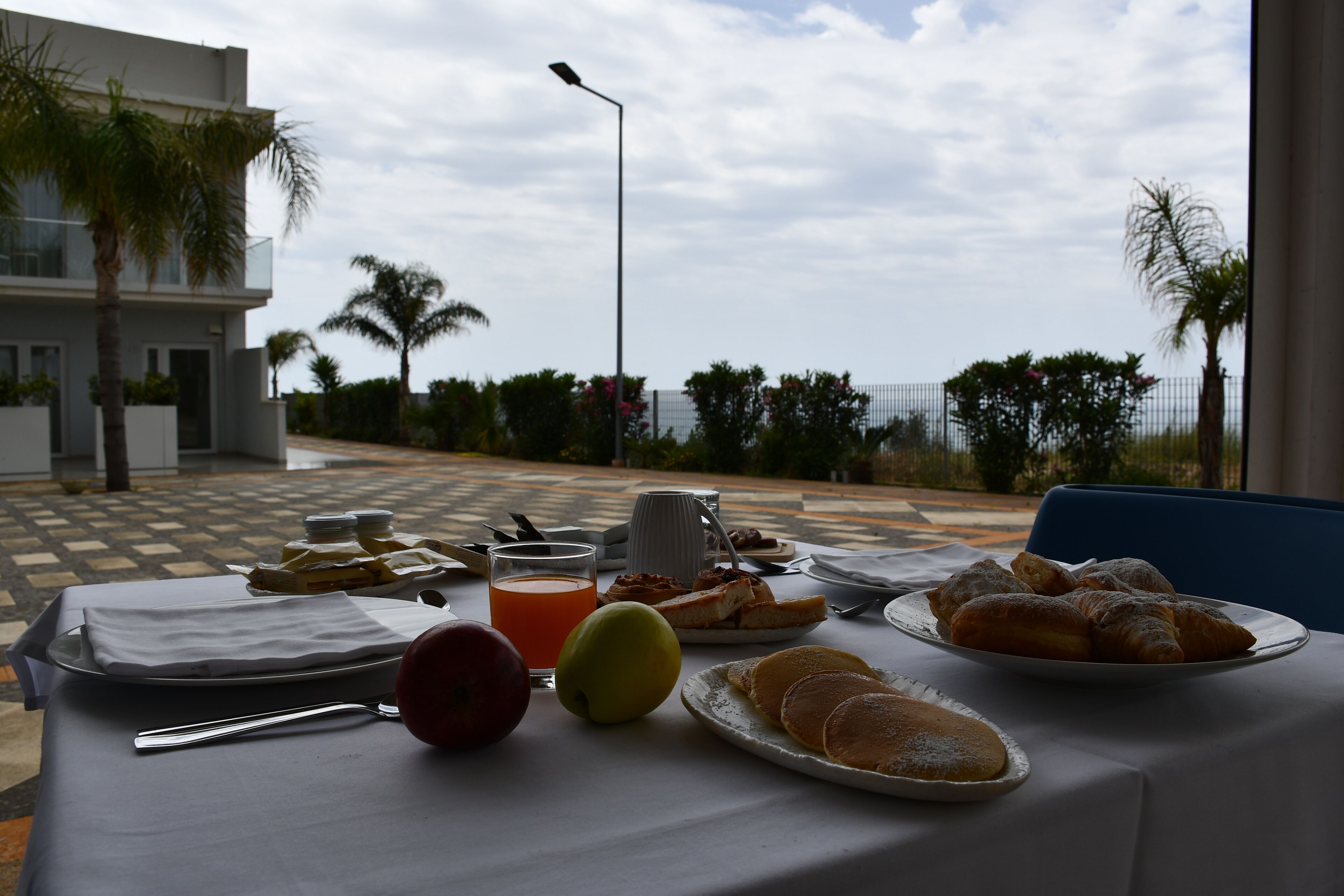 Una mesa de desayuno con diversos alimentos, un frutero y un vaso de jugo de naranja.